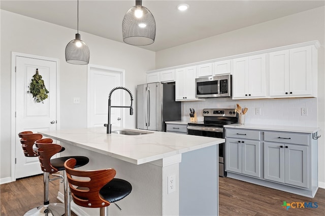 kitchen with a center island with sink, sink, appliances with stainless steel finishes, dark hardwood / wood-style floors, and pendant lighting