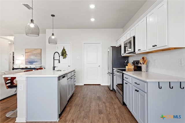 kitchen with stainless steel appliances, wood-type flooring, sink, an island with sink, and pendant lighting