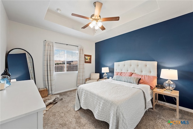 carpeted bedroom with ceiling fan and a tray ceiling