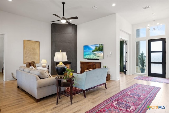 living area featuring visible vents, baseboards, light wood-style flooring, ceiling fan with notable chandelier, and a high ceiling