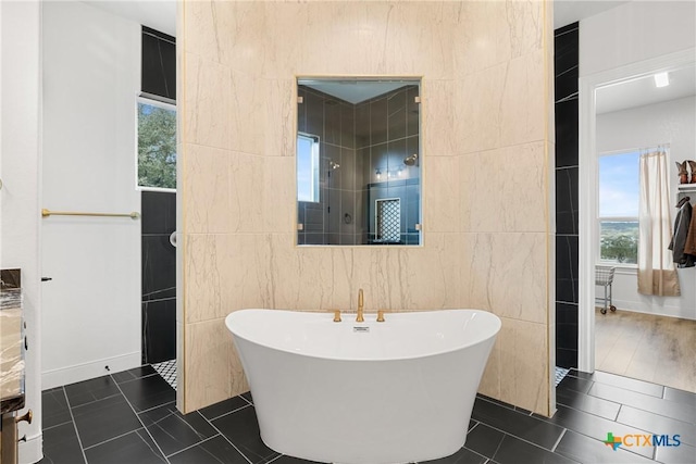 bathroom featuring tile patterned flooring, a freestanding bath, and tile walls