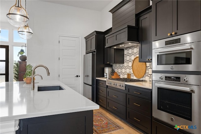 kitchen with light countertops, decorative backsplash, light wood-style flooring, appliances with stainless steel finishes, and a sink