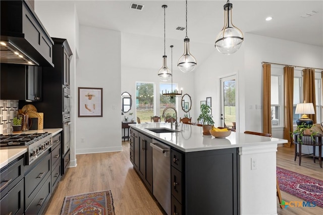 kitchen with visible vents, stainless steel appliances, a sink, light countertops, and wall chimney exhaust hood