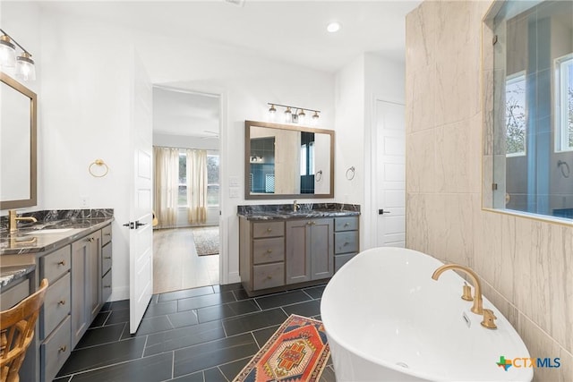 full bathroom featuring tile patterned floors, two vanities, a sink, tile walls, and a soaking tub