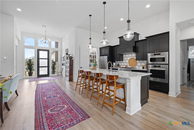 kitchen featuring backsplash, light countertops, appliances with stainless steel finishes, a large island, and dark cabinets