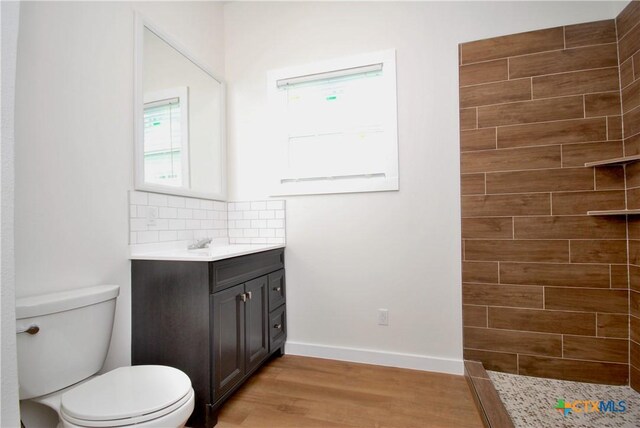 215 E Gonzales St, Yoakum, TX 77995 - full bath featuring vanity, tasteful backsplash, toilet, a tile shower, and wood finished floors