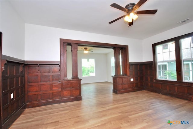 215 E Gonzales St, Yoakum, TX 77995 - unfurnished living room featuring light wood-style flooring, visible vents, decorative columns, a ceiling fan, and wainscoting