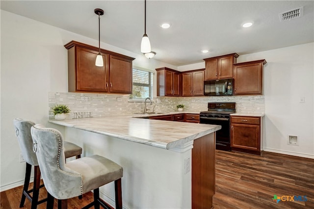 kitchen with kitchen peninsula, pendant lighting, black appliances, and a breakfast bar