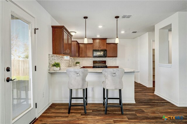 kitchen with sink, dark hardwood / wood-style flooring, pendant lighting, a breakfast bar area, and black appliances