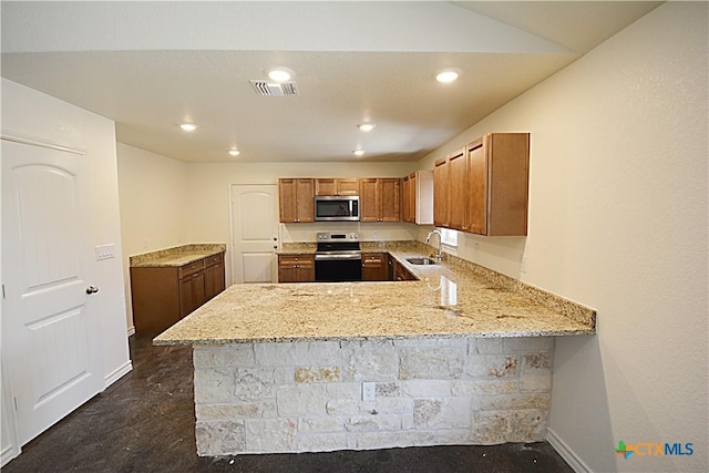 kitchen with appliances with stainless steel finishes, kitchen peninsula, sink, and light stone countertops