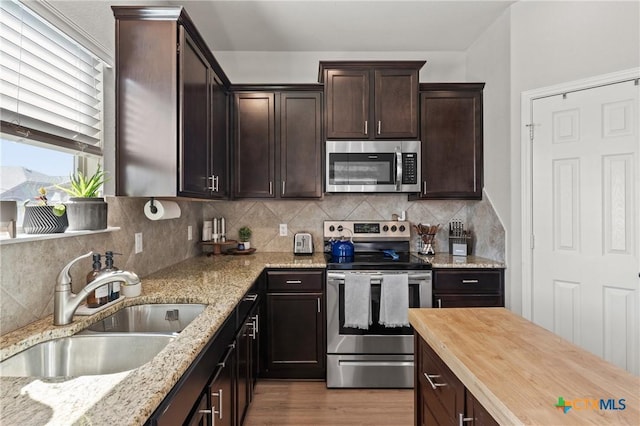 kitchen featuring dark brown cabinetry, a sink, light wood-style floors, appliances with stainless steel finishes, and light stone countertops