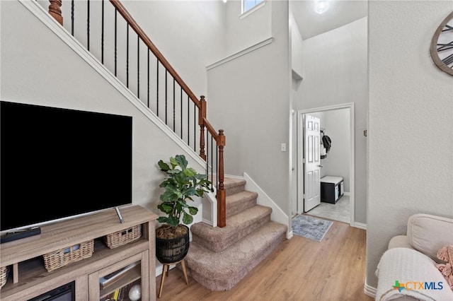 foyer entrance featuring baseboards, a high ceiling, stairway, and light wood finished floors