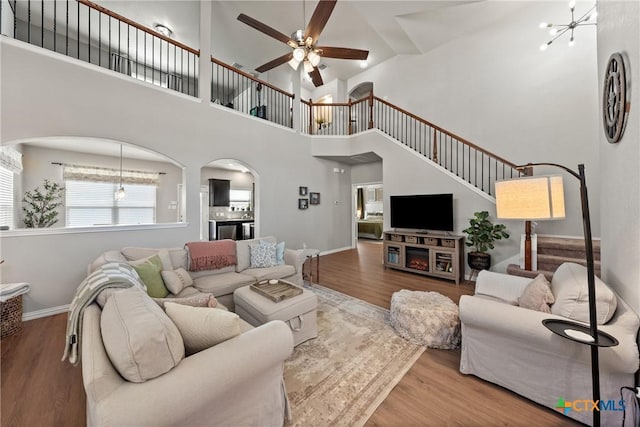 living area featuring stairs, ceiling fan with notable chandelier, wood finished floors, and baseboards