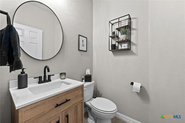 half bath with baseboards, a textured wall, vanity, and toilet