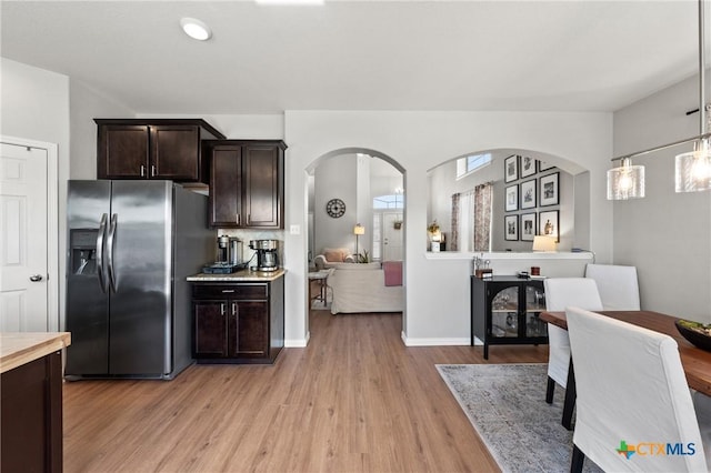 kitchen with dark brown cabinetry, arched walkways, stainless steel fridge with ice dispenser, decorative light fixtures, and light countertops