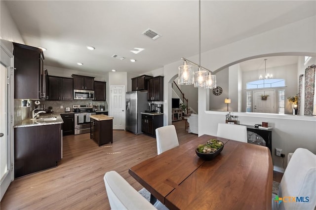 dining space featuring arched walkways, a notable chandelier, light wood finished floors, visible vents, and stairway