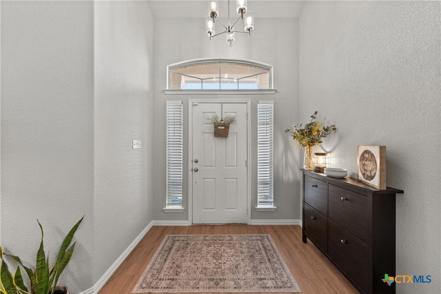 entrance foyer featuring a notable chandelier, a textured wall, light wood finished floors, and baseboards