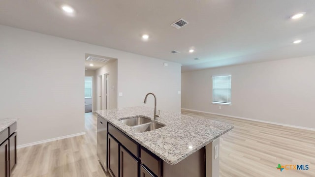 kitchen featuring a kitchen island with sink, sink, stainless steel dishwasher, light hardwood / wood-style floors, and light stone counters