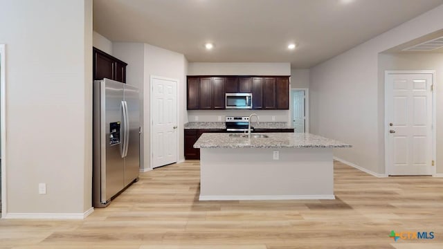 kitchen with light stone countertops, sink, stainless steel appliances, light hardwood / wood-style floors, and a kitchen island with sink