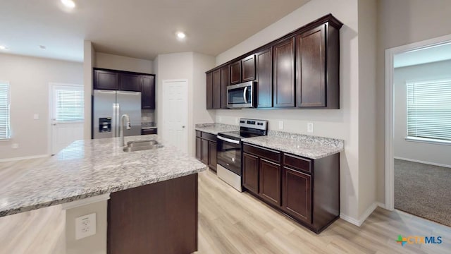 kitchen with a center island with sink, sink, light hardwood / wood-style flooring, dark brown cabinets, and stainless steel appliances