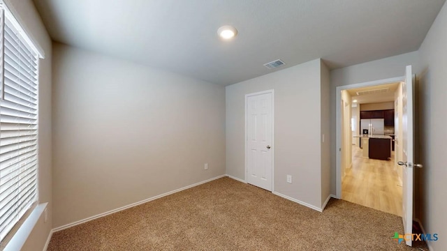 unfurnished bedroom featuring light carpet and stainless steel refrigerator with ice dispenser