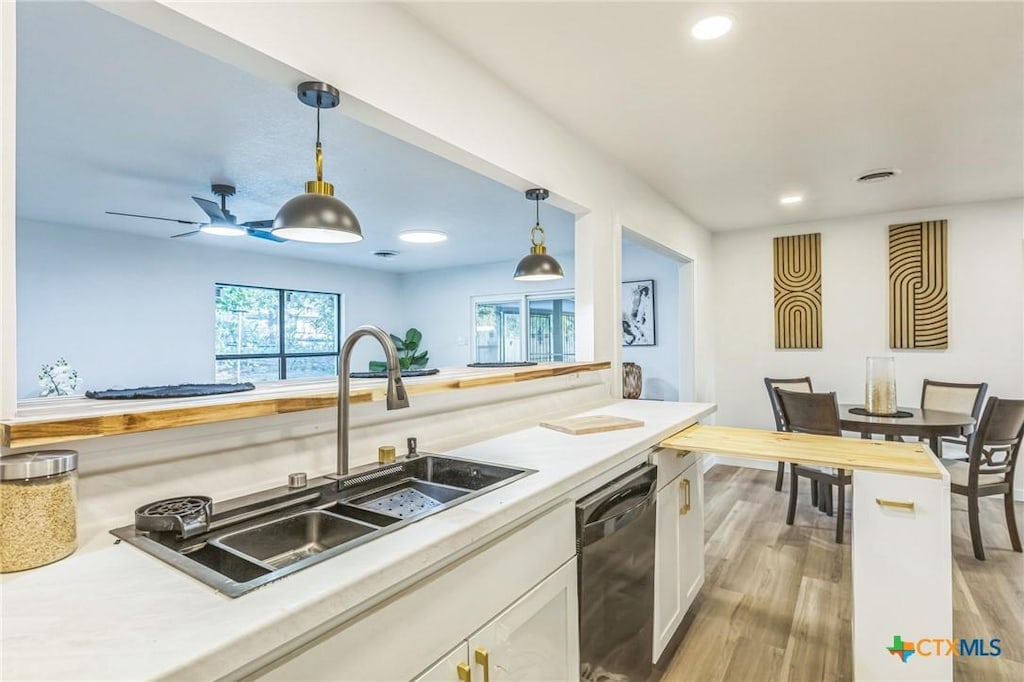 kitchen featuring sink, light wood-type flooring, black dishwasher, pendant lighting, and white cabinets