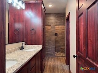 133 E Mcanelly St, Lometa, TX 76853 - bathroom featuring double vanity, a tile shower, and wood finished floors