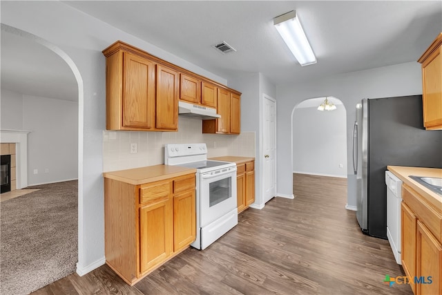 kitchen with dark wood-type flooring, white appliances, a tile fireplace, and backsplash