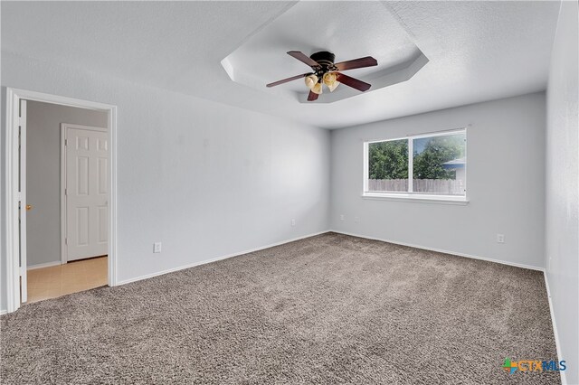 carpeted empty room with a textured ceiling, ceiling fan, and a raised ceiling