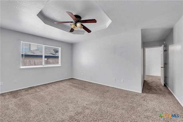 empty room featuring a textured ceiling, carpet floors, ceiling fan, and a raised ceiling