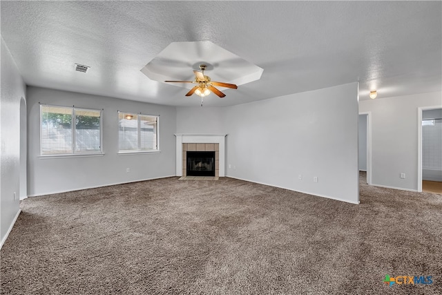 unfurnished living room featuring ceiling fan, a textured ceiling, a tiled fireplace, and carpet floors