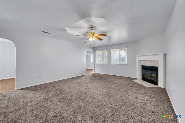 unfurnished living room with ceiling fan, a tiled fireplace, a textured ceiling, and carpet flooring