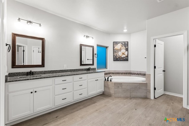 bathroom featuring wood-type flooring, vanity, and tiled tub