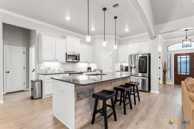 kitchen featuring appliances with stainless steel finishes, dark stone countertops, an island with sink, and light hardwood / wood-style flooring