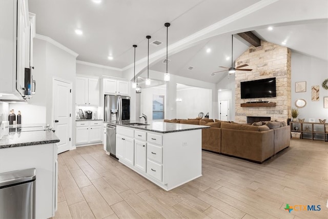 kitchen with white cabinetry, appliances with stainless steel finishes, an island with sink, and vaulted ceiling with beams