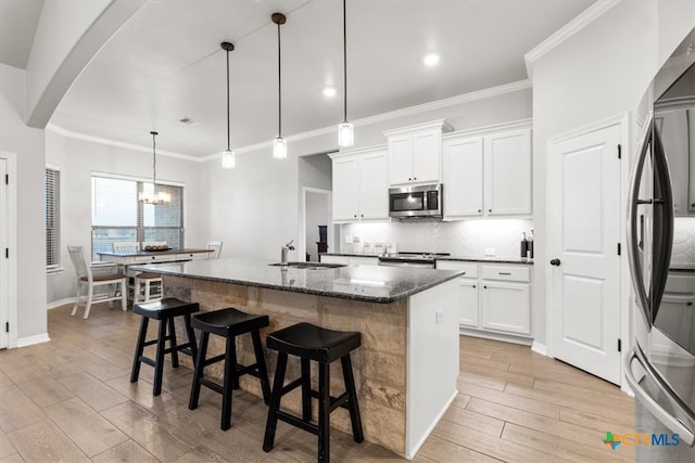 kitchen with stainless steel appliances, hanging light fixtures, sink, an island with sink, and white cabinets