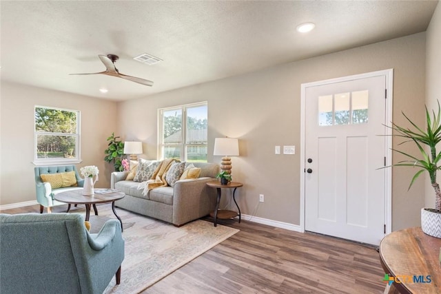 living room with a wealth of natural light, visible vents, wood finished floors, and ceiling fan