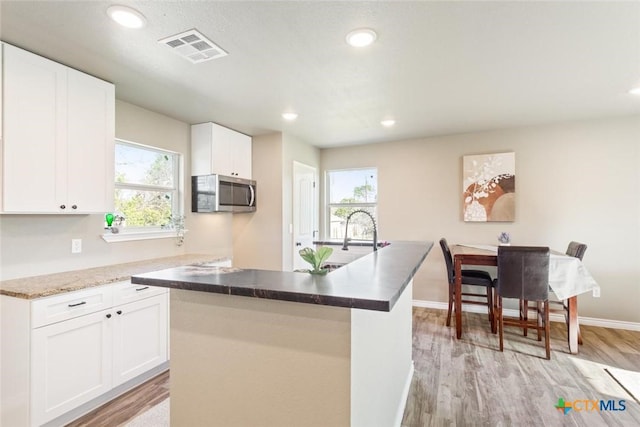 kitchen featuring visible vents, light wood-style flooring, a sink, white cabinetry, and stainless steel microwave