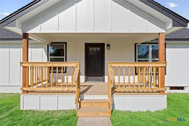 view of exterior entry with a porch, a lawn, board and batten siding, and roof with shingles