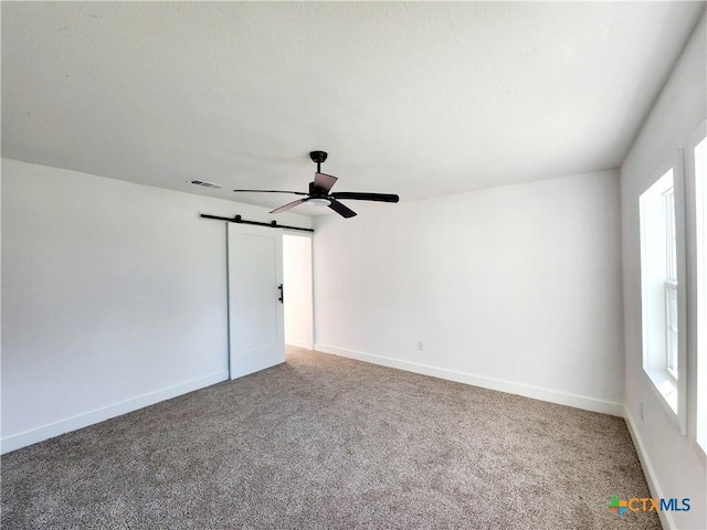 carpeted spare room with a ceiling fan, baseboards, a barn door, and visible vents