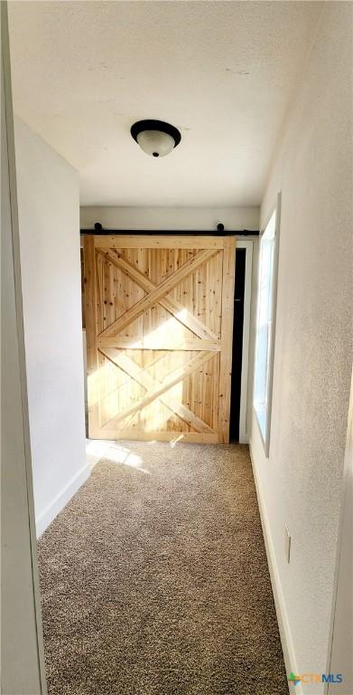 hall featuring baseboards, carpet floors, a textured ceiling, and a barn door