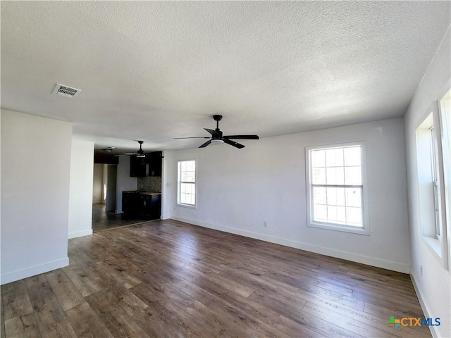 unfurnished living room with dark wood-style flooring, baseboards, ceiling fan, and visible vents
