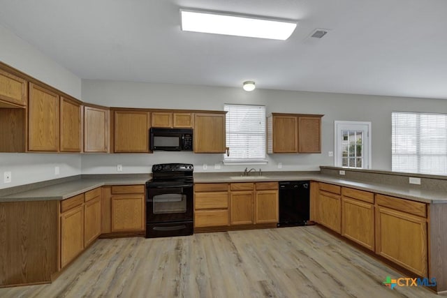 kitchen with kitchen peninsula, sink, light hardwood / wood-style floors, and black appliances