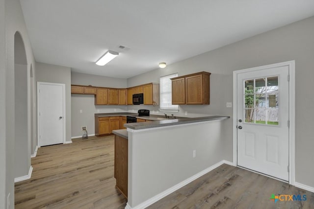 kitchen with black appliances, plenty of natural light, light wood-type flooring, and kitchen peninsula