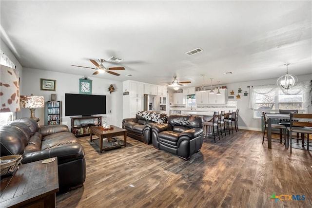 living room featuring ceiling fan with notable chandelier and dark wood-type flooring