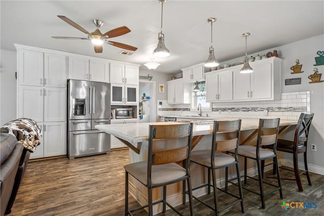 kitchen featuring white cabinetry, a kitchen bar, hanging light fixtures, stainless steel appliances, and light stone countertops