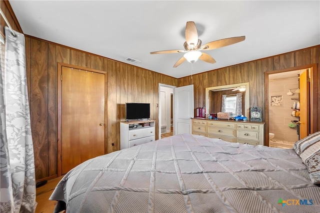 bedroom featuring ensuite bathroom, ceiling fan, and wood walls