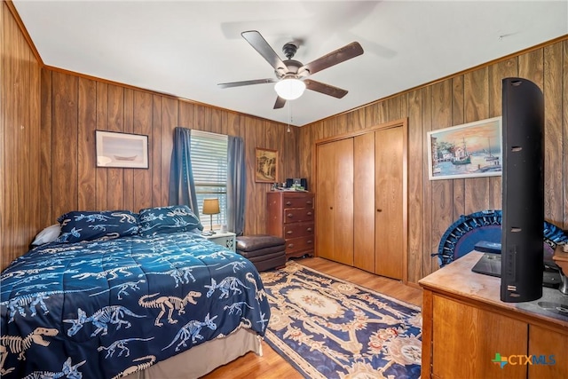 bedroom with ceiling fan, wooden walls, light wood-type flooring, and a closet