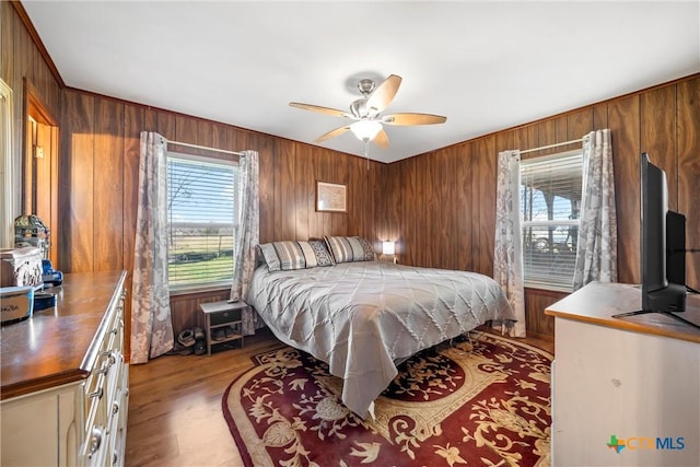 bedroom featuring ceiling fan, light hardwood / wood-style floors, and wood walls