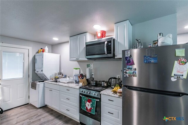2518 Marlandwood Rd, Temple, TX 76502 - kitchen with white cabinets, light wood finished floors, stacked washer and dryer, and appliances with stainless steel finishes